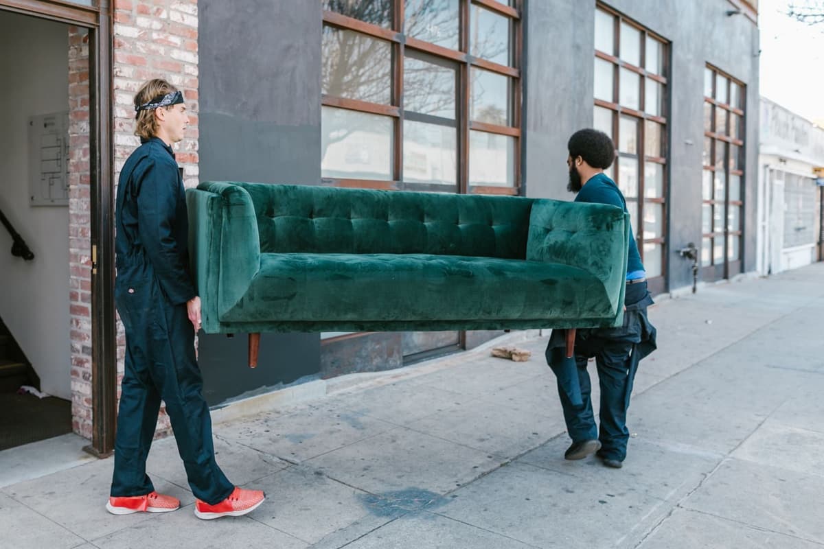 Two movers carrying a green sofa out of a building onto the sidewalk