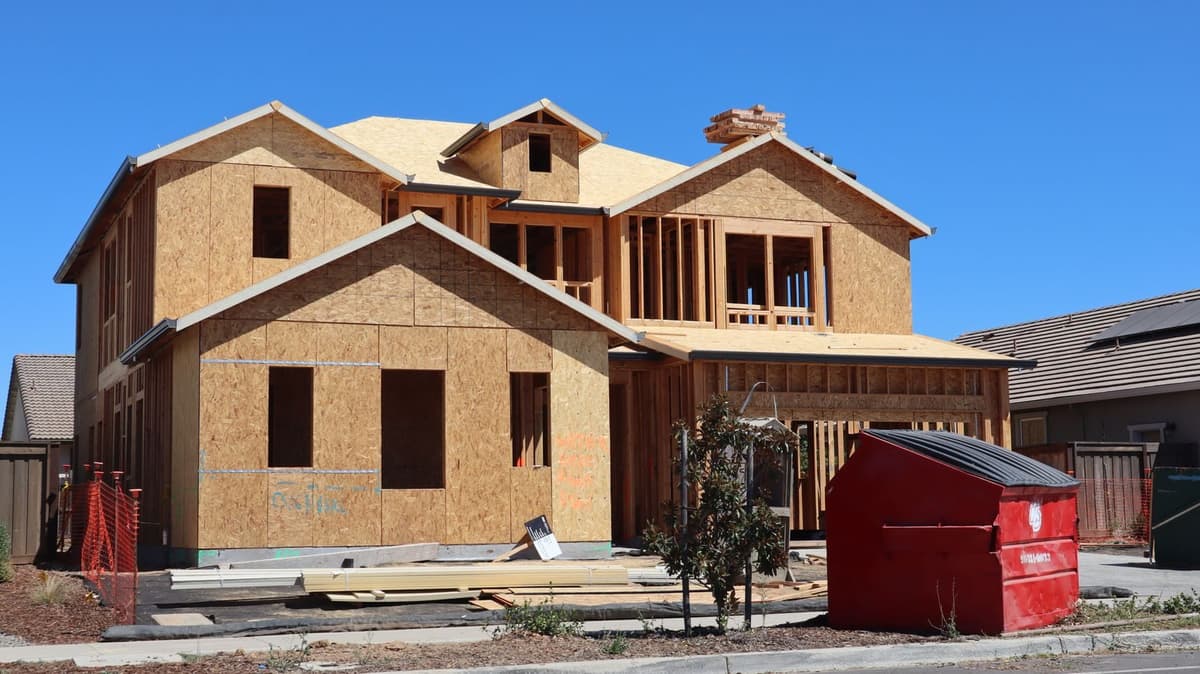 Framed new-construction house with a dumpster on site